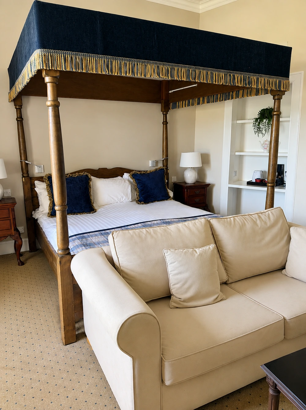 Four-poster bedroom with navy canopy, traditional furnishings and seating area at Tulloch Castle, Dingwall, Scotland.
