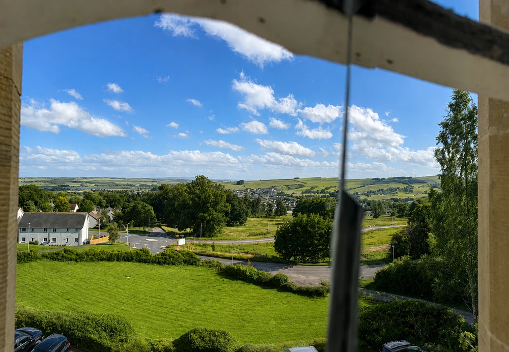 View across the Scottish countryside from Tulloch Castle in Dingwall, with rolling green hills beneath a blue summer sky.
