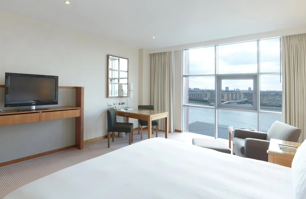 Bright bedroom at Canary Riverside Plaza Hotel in London with floor-to-ceiling windows and views across the River Thames.