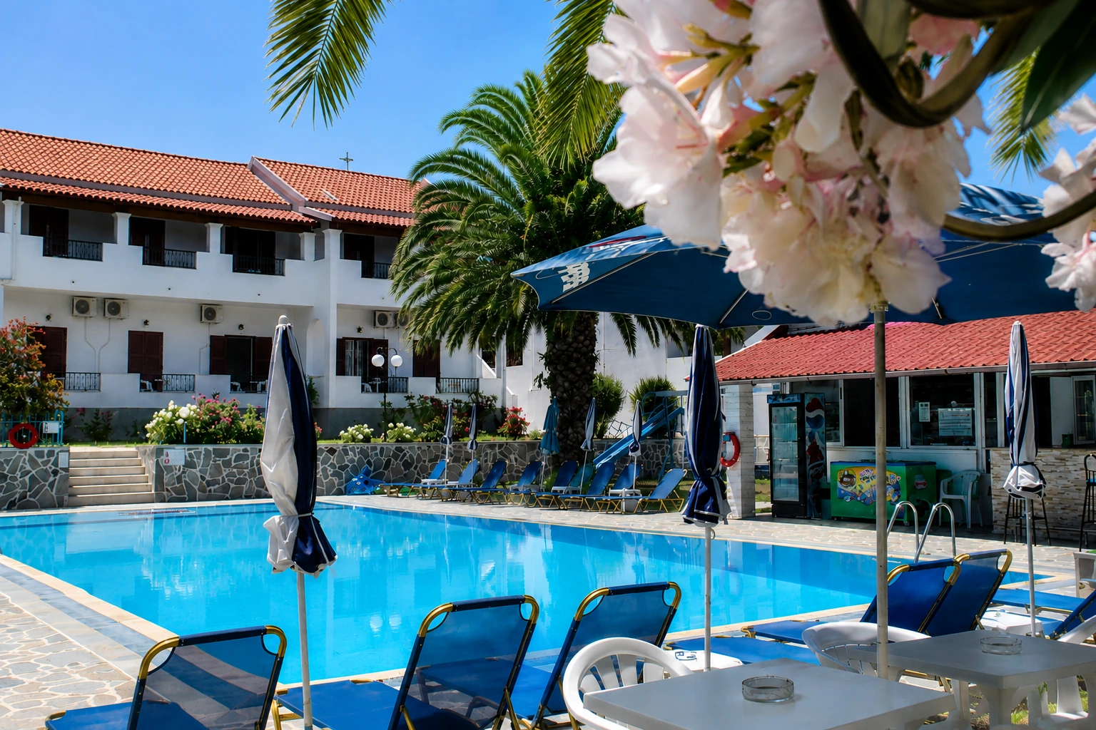 Swimming pool and poolside terrace at Tria Adelphia in Arillas, Corfu, surrounded by palm trees and traditional Greek-style accommodation.
